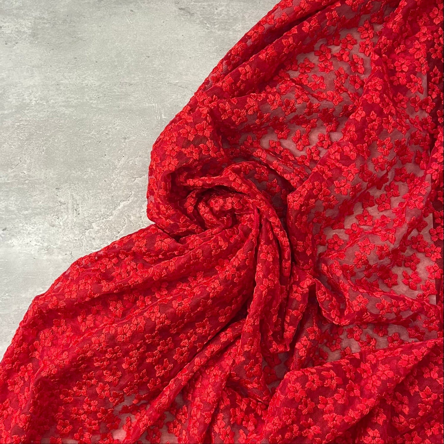 Red floral embroidered tulle fabric by Tiss'ART, showcasing intricate flower designs and delicate texture.